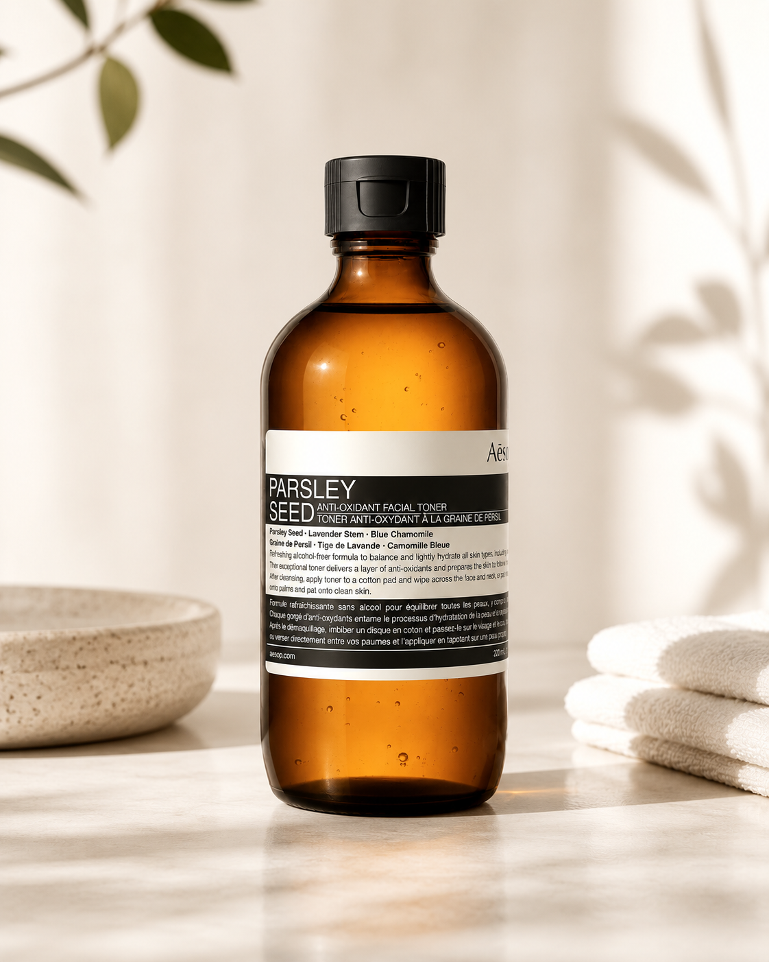 Aesop Parsley Seed Anti-Oxidant Facial Toner displayed on a light stone countertop in a minimalist spa-inspired setting with soft natural sunlight, a ceramic bowl, folded white towels, and botanical shadows. The calming composition highlights the antioxidant-rich facial toner as part of a premium skincare routine, emphasizing gentle hydration, skin balancing, and preparation for moisturizing while reinforcing Aesop's clean apothecary aesthetic.