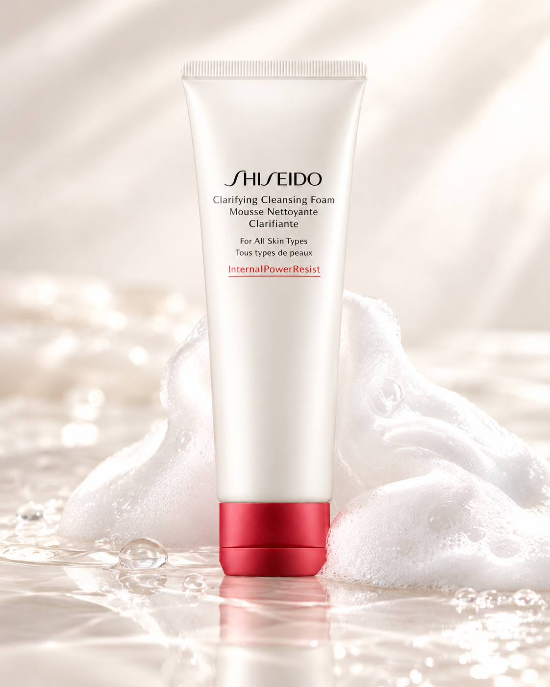 Shiseido Clarifying Cleansing Foam in a white tube with a metallic red cap, surrounded by luxurious white foam, delicate bubbles and water reflections. Premium facial cleanser for all skin types, presented in a soft neutral skincare setting that highlights its rich, creamy texture.